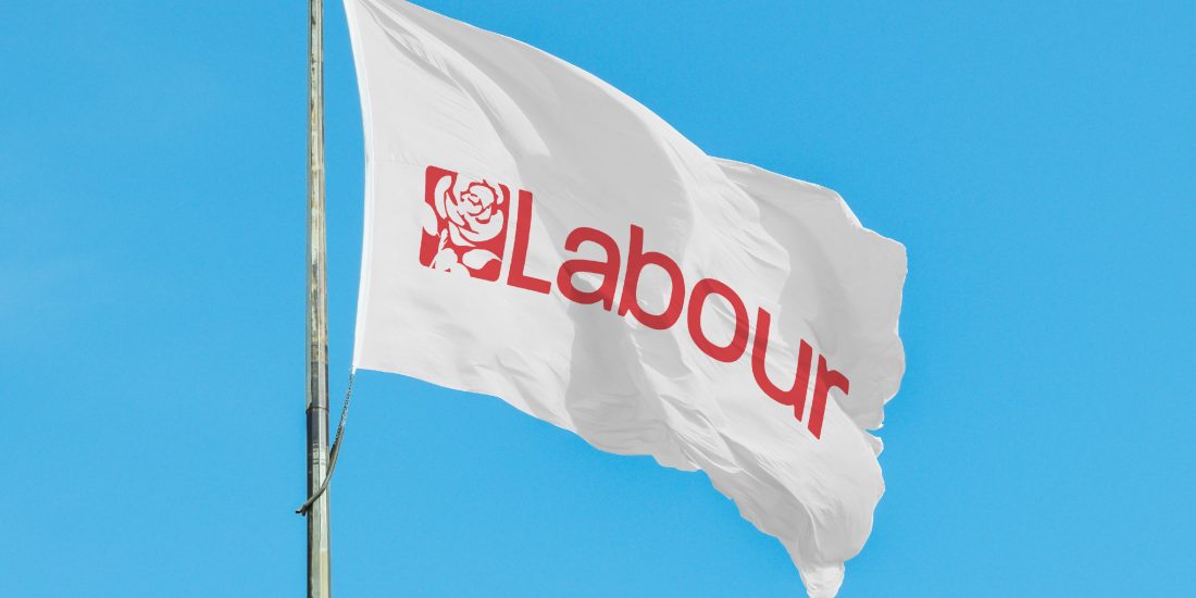 Labour Party flag waving in the wind, infront of a bright blue sky